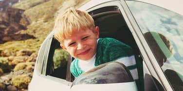 Smiling child leaning out of a car window during a road trip