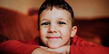 A young boy resting his chin on his arms with a calm, content smile, reflecting the emotional safety and secure attachment that come from feeling deeply loved at home