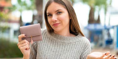 woman faking wealth holding a wallet and shrugging