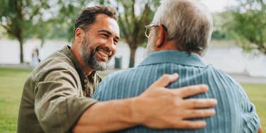 Adult son placing a reassuring arm around his father during a calm moment of family reconciliation outdoors.