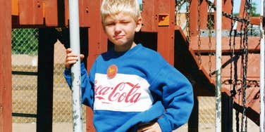 Child on a playground in a Ninties-style Coca-Cola sweatshirt