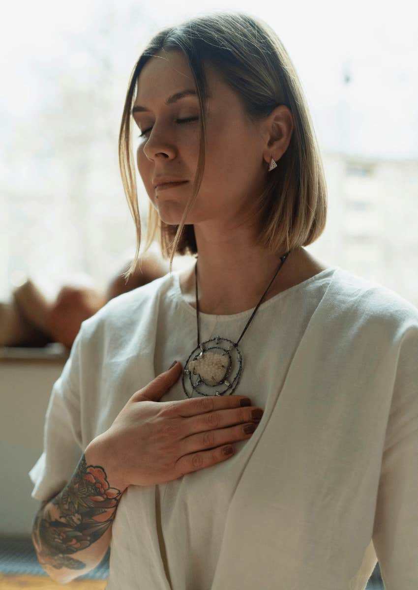 peaceful young woman holding her hand to her chest