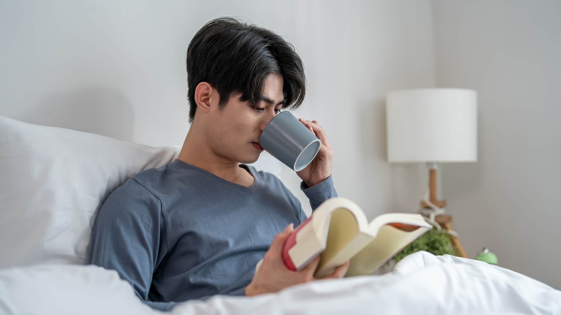 man reading while drinking coffee in bed