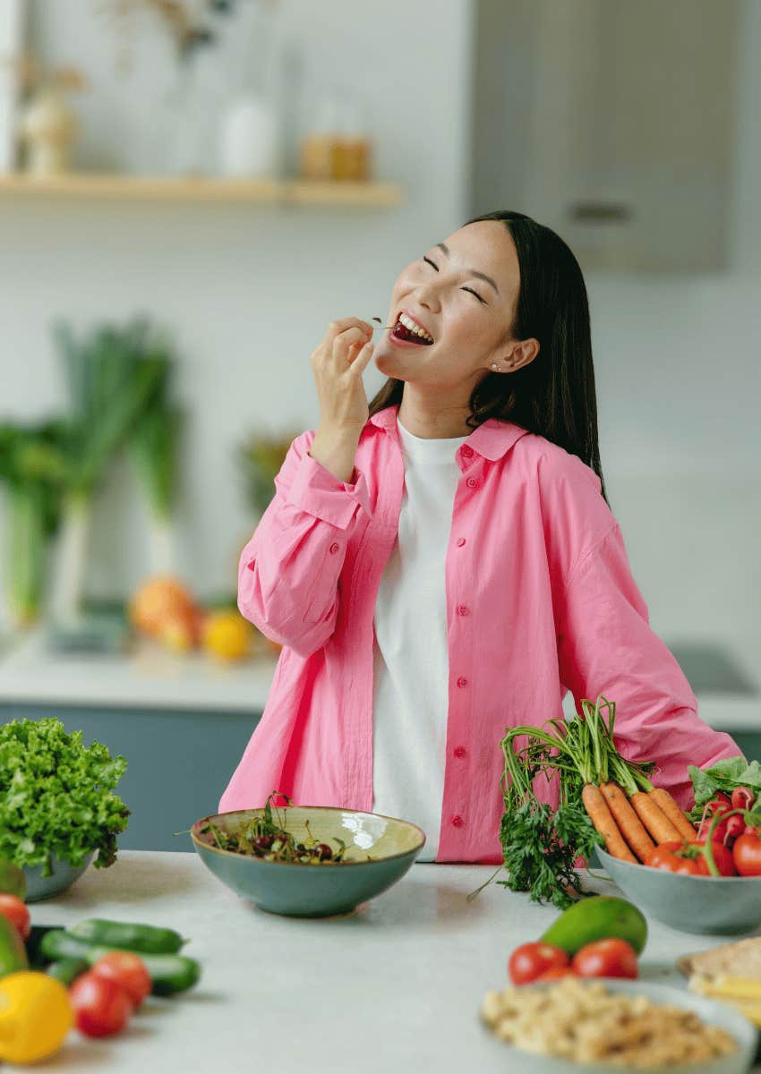 smiling woman standing in kitchen with vegetables