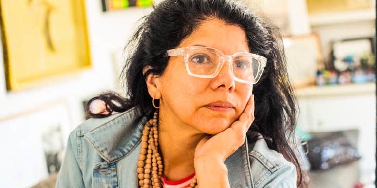 Woman with glasses resting her face in her hand, looking thoughtful while sitting indoors.