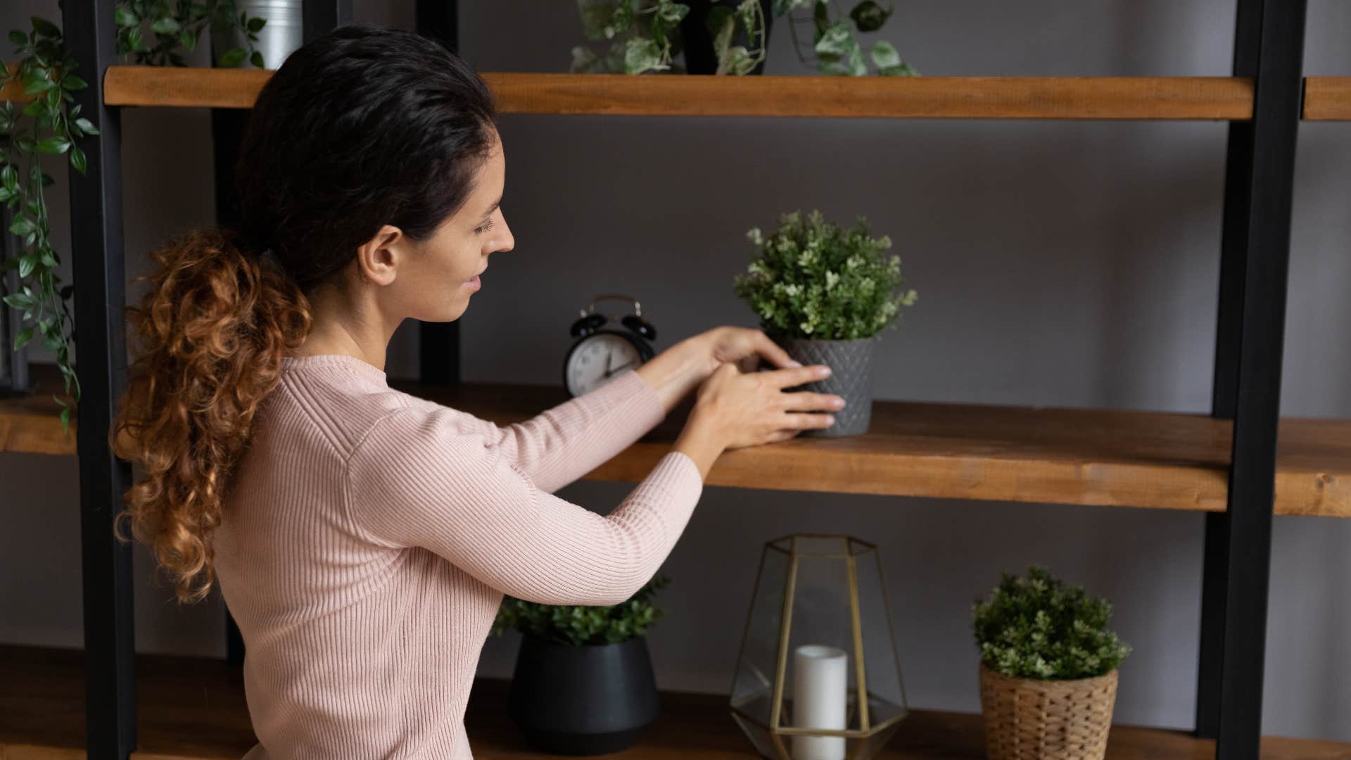 woman placing plant on wood shelf in living room