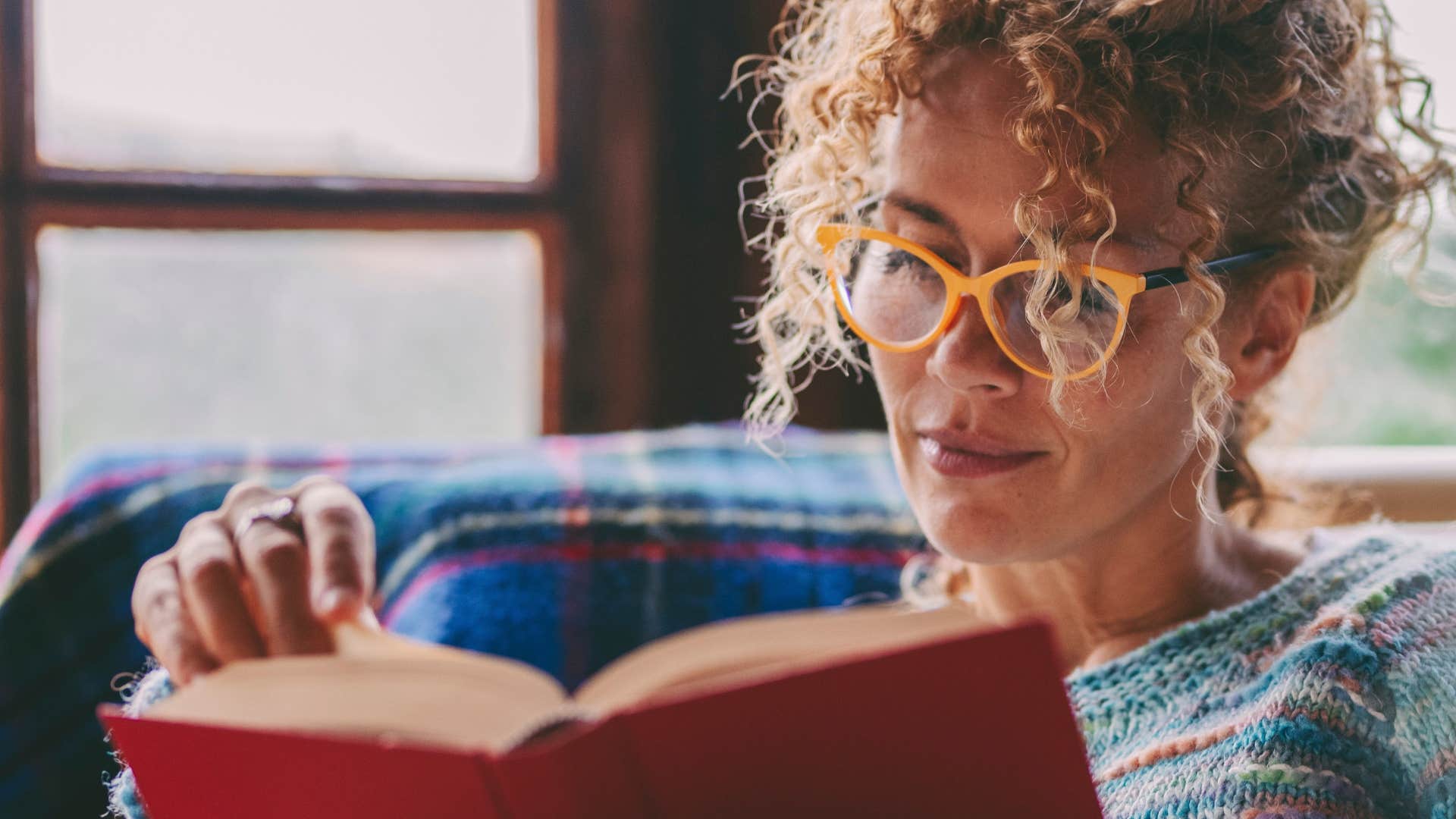 intelligent woman reading a long book on her couch